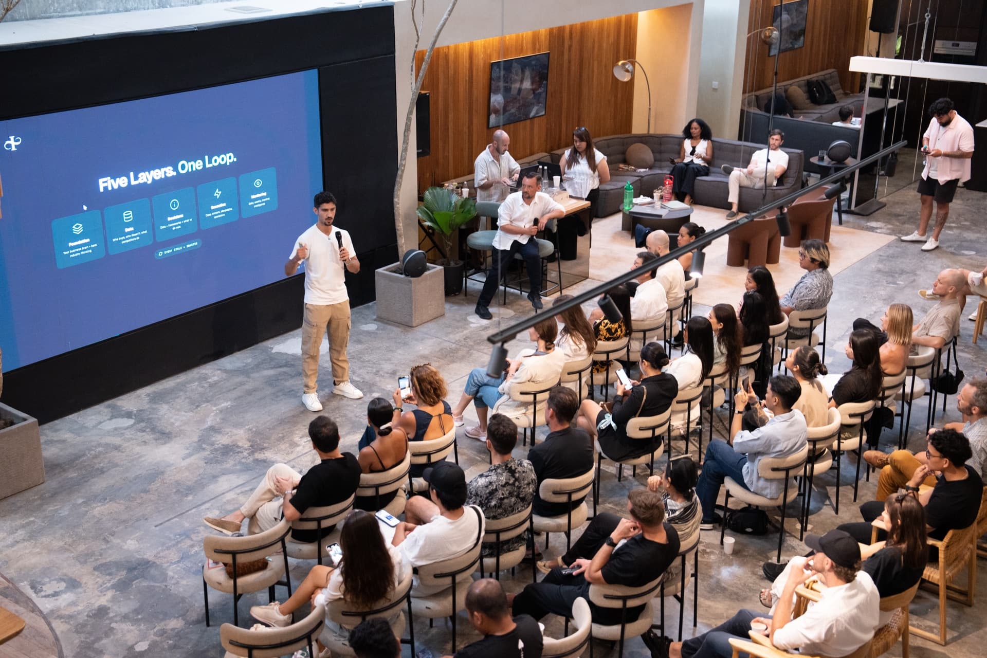 A full room at an Imperium mastermind, the five layers of the AI Operating System on the screen.